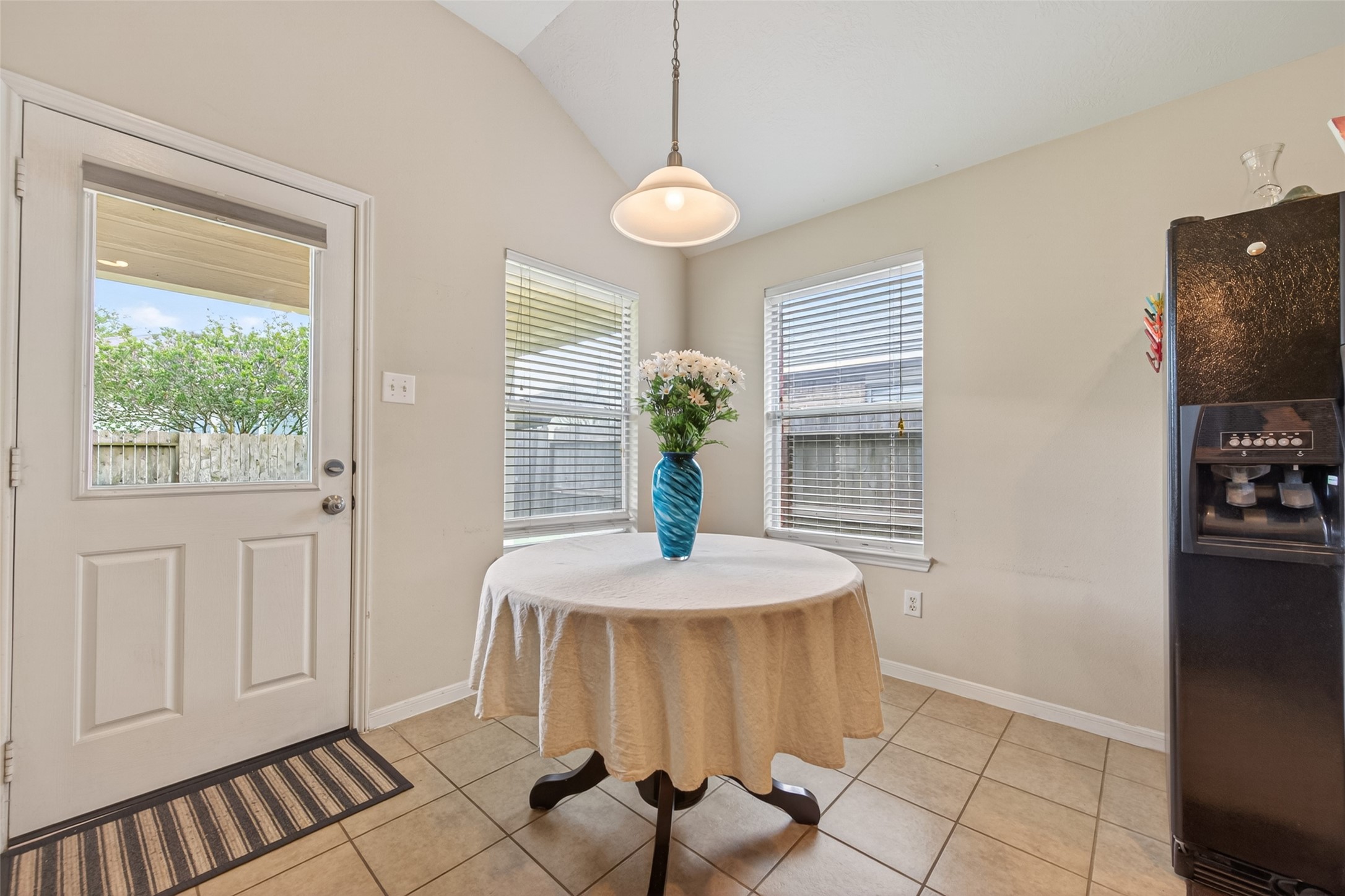 8622 Henrico Lane Rosenberg, TX 77469 - Photo 10 of 20 Bright kitchen nook with tiled floor, featuring a round table with a decorative centerpiece. Large windows provide natural light, and there's access to the backyard. A black refrigerator is positioned to the side.