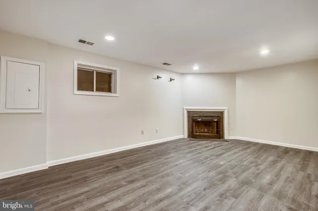 a view of an empty room with wooden floor fireplace and a window