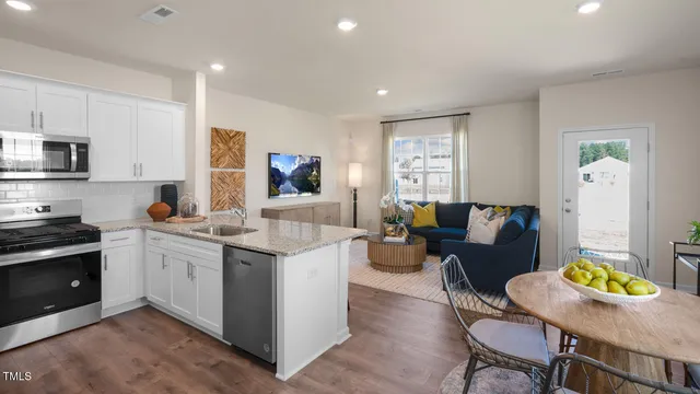 a living room with stainless steel appliances kitchen island granite countertop a stove a sink a dining table and chairs