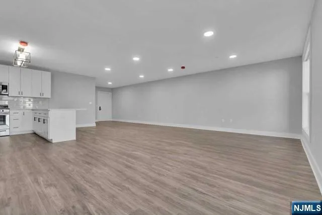 a view of an empty room with wooden floor and kitchen