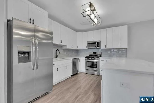 a kitchen with stainless steel appliances granite countertop a refrigerator a stove oven a sink dishwasher and white cabinets with wooden floor