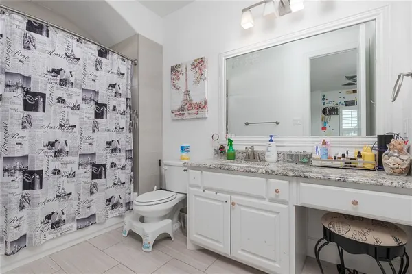 a bathroom with a granite countertop toilet a sink a mirror a window and a shower