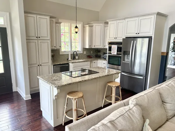 a kitchen with stainless steel appliances granite countertop a refrigerator a stove a sink and white cabinets with wooden floor