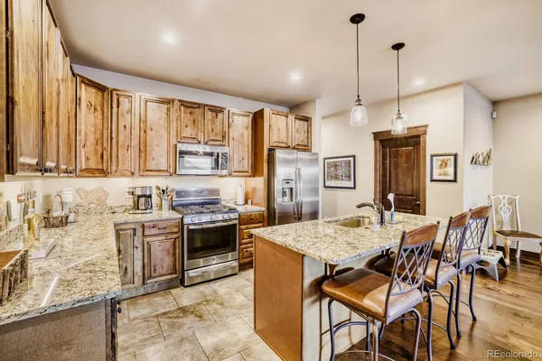 a kitchen with stainless steel appliances granite countertop a stove top oven a sink a dining table and chairs with wooden floor