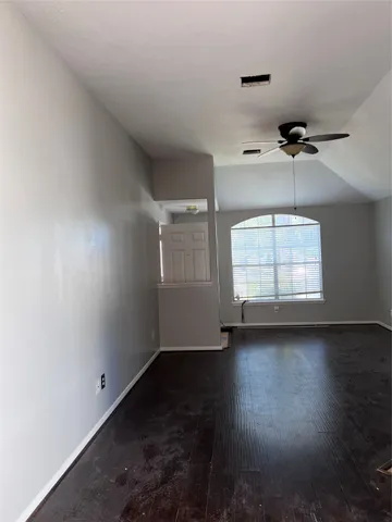 an empty room with wooden floor ceiling fan and windows