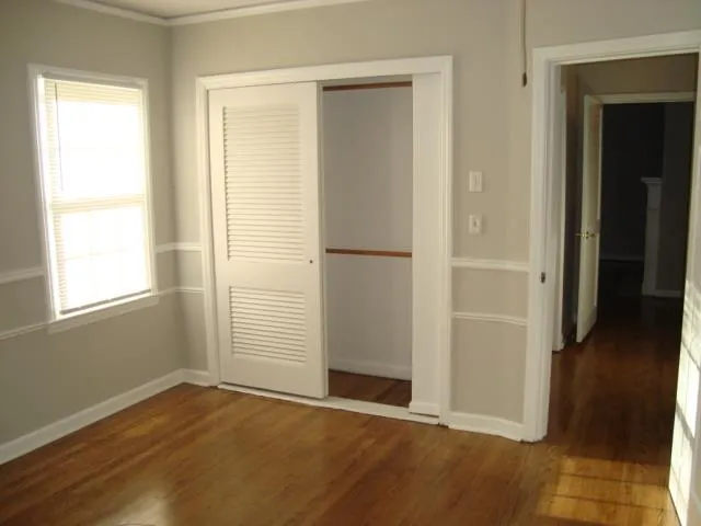 an empty room with wooden floor closet and windows