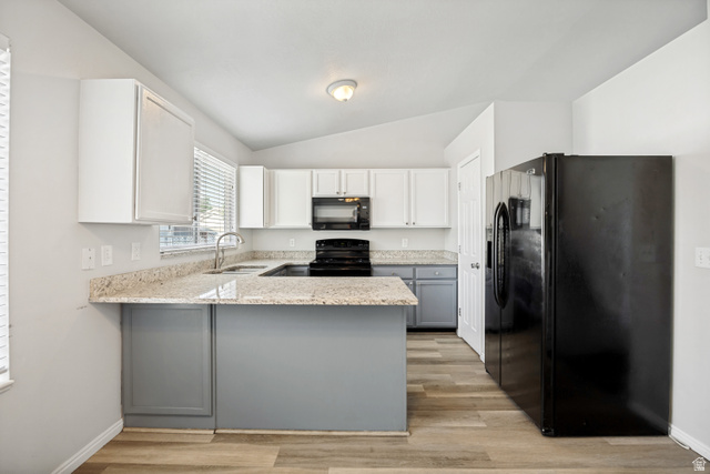 5529 Ridge Hollow Way Kearns, UT 84118 - Photo 6 of 23 Modern kitchen featuring light wood-finish flooring, two-tone cabinetry, U-shaped countertops, stainless steel sink, and black appliances