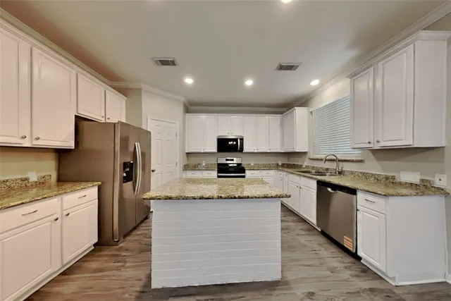 a kitchen with stainless steel appliances granite countertop a stove top oven a refrigerator a sink and dishwasher with wooden floor