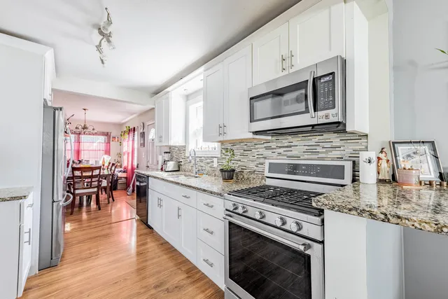 a kitchen with stainless steel appliances kitchen island granite countertop a stove top oven a sink a dining table and chairs with wooden floor