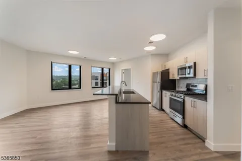 a view of kitchen with stainless steel appliances granite countertop a stove top oven a sink dishwasher a refrigerator and a dining table with wooden floor