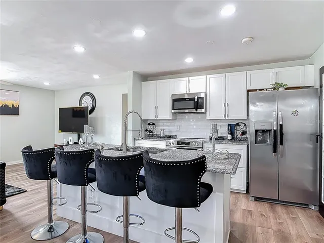 a kitchen with stainless steel appliances kitchen island granite countertop a refrigerator a stove a sink counter tops and chairs with wooden floor