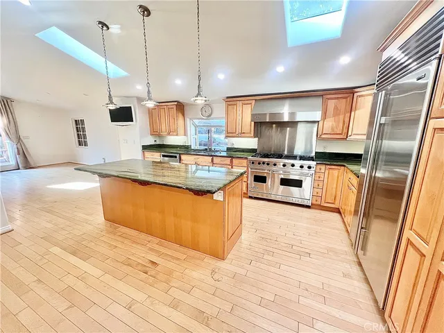 a large kitchen with stainless steel appliances kitchen island granite countertop a stove top oven a sink dishwasher a dining table and chairs with wooden floor