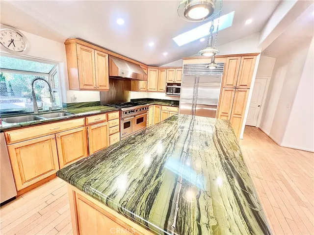 a view of a kitchen with kitchen island a sink wooden floor and stainless steel appliances
