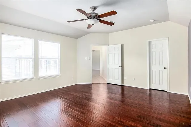 an empty room with wooden floor fan and windows