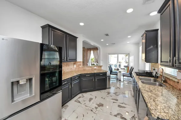 a kitchen with stainless steel appliances kitchen island granite countertop a refrigerator a stove a sink a dining table and chairs with wooden floor