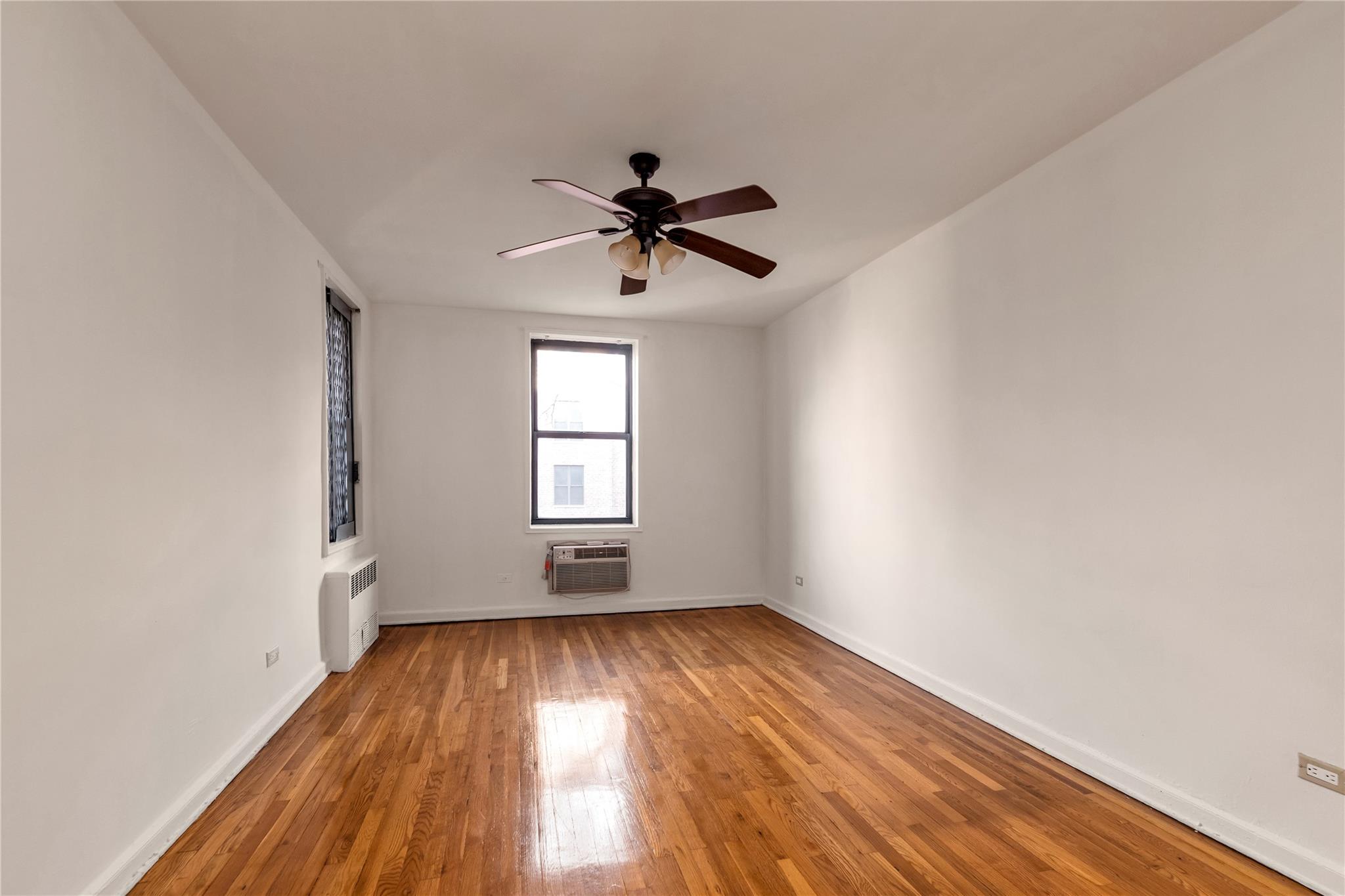 141-05 Pershing Crescent, Unit 210 Queens, NY 11435 - Photo 17 of 22 Empty room featuring a wall mounted air conditioner, radiator heating unit, hardwood / wood-style flooring, and ceiling fan