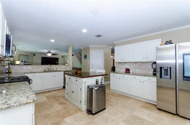 a kitchen with stainless steel appliances granite countertop a stove top oven a sink a dining table and chairs with white cabinets