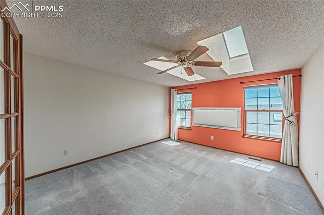 an empty room with chandelier fan and windows
