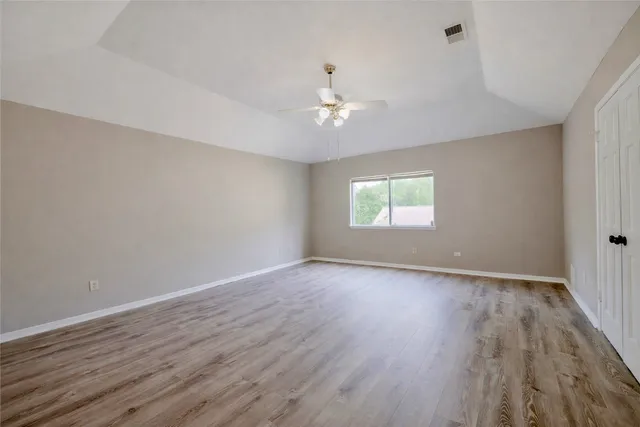 an empty room with wooden floor chandelier fan and windows