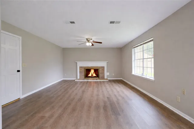 a view of an empty room with wooden floor fireplace and a window