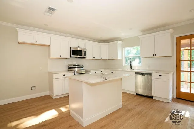 a kitchen with stainless steel appliances a stove top oven a sink a refrigerator white cabinets and wooden floor