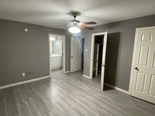 a view of an empty room with wooden floor and a ceiling fan
