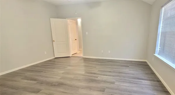 a view of an empty room with wooden floor and a window