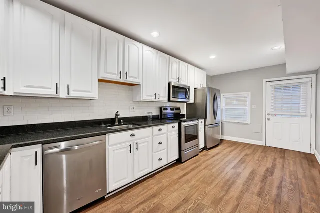 a large kitchen with granite countertop a stove top oven a sink dishwasher and a refrigerator with wooden floor