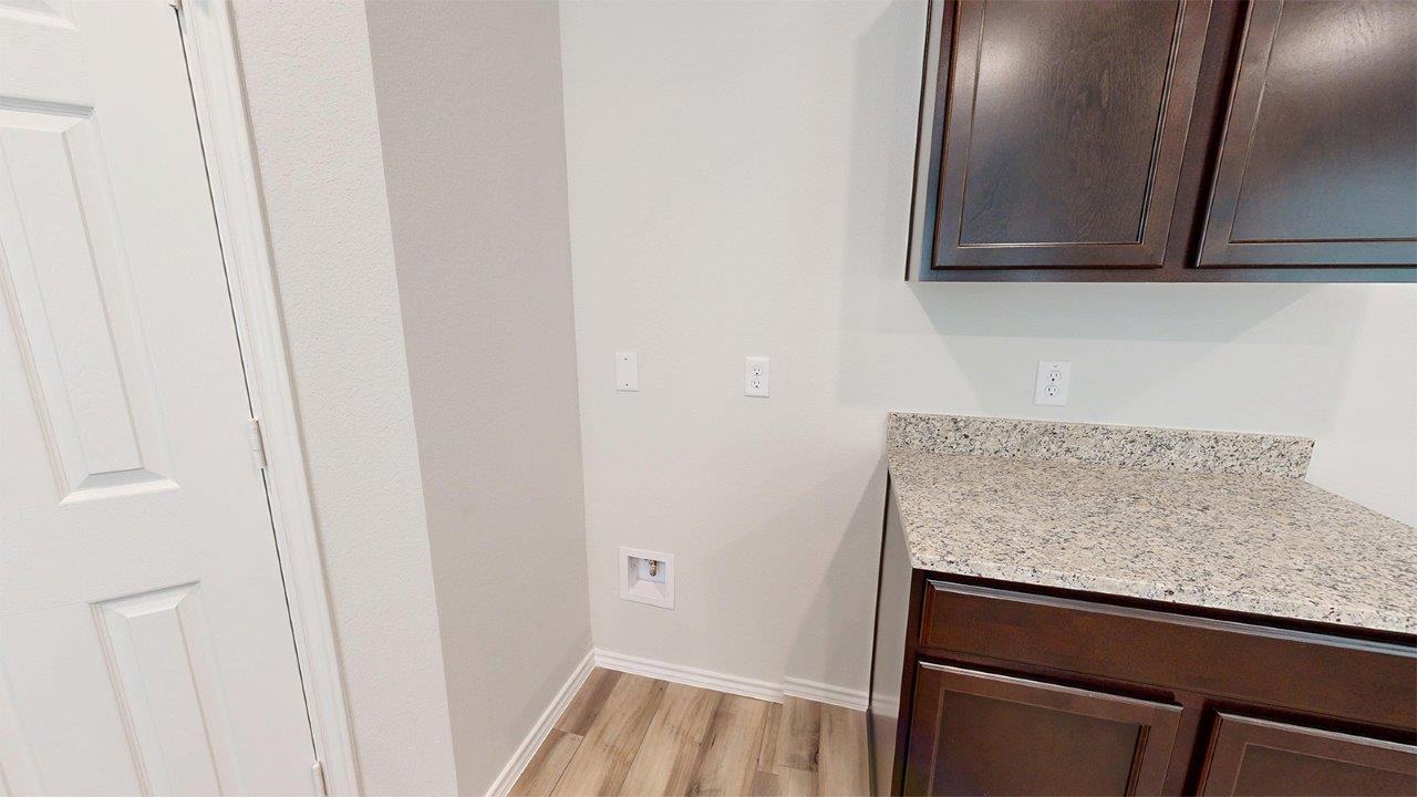 557 Hector Loop Georgetown, TX 78626 - Photo 6 of 38 Utility area featuring wood-finish flooring, dark wood cabinetry, and a light speckled countertop