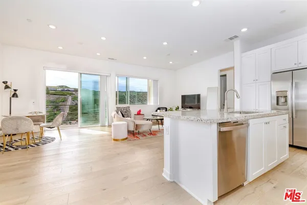 a kitchen with stainless steel appliances granite countertop a stove top oven a sink dishwasher a dining table and chairs with wooden floor