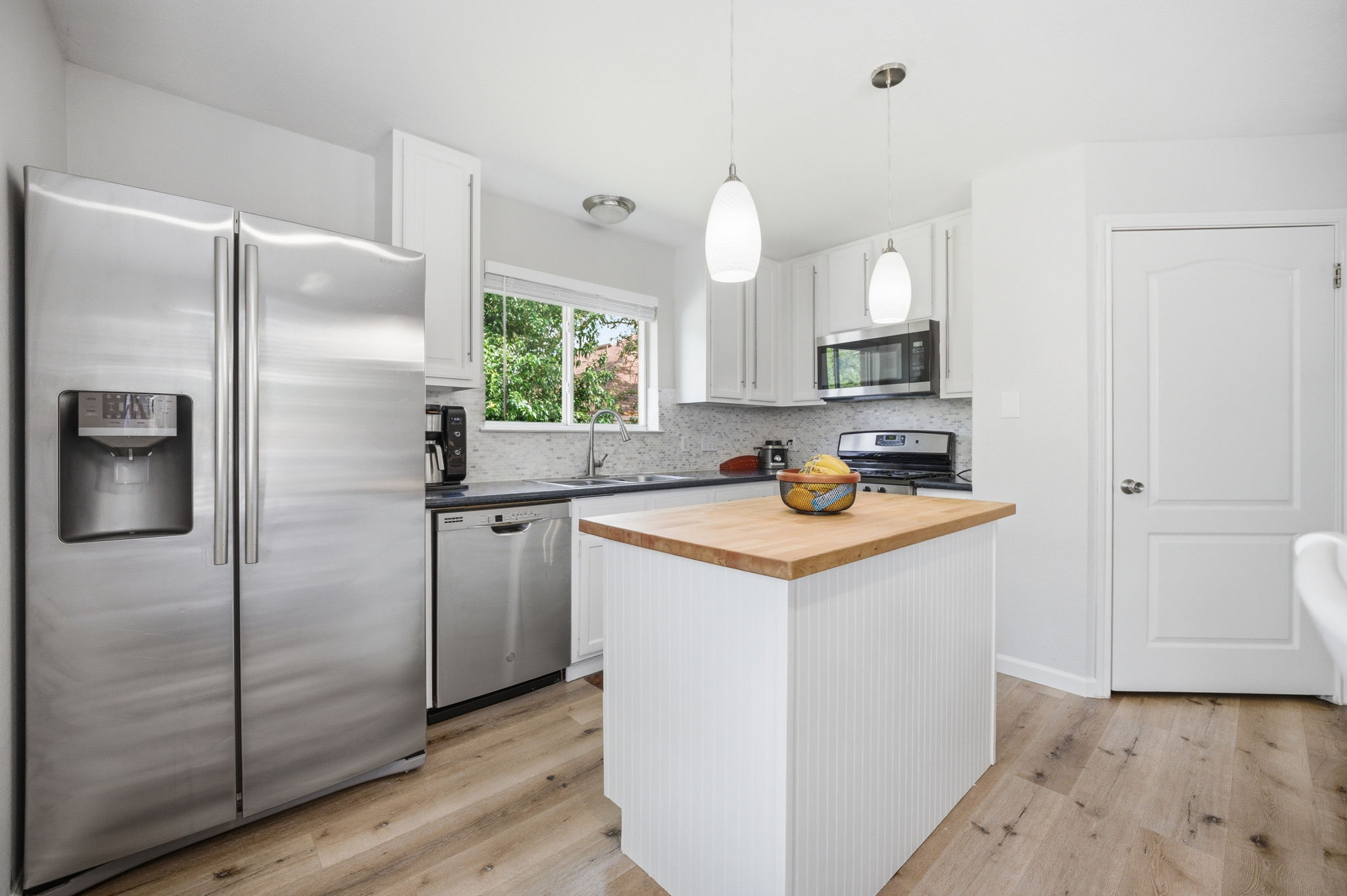 9024 Heiden Lane Austin, TX 78749 - Photo 11 of 28 Bright kitchen featuring white cabinetry, stainless steel appliances, a center island with a wood-finish countertop, wood-finish flooring, and pendant lighting