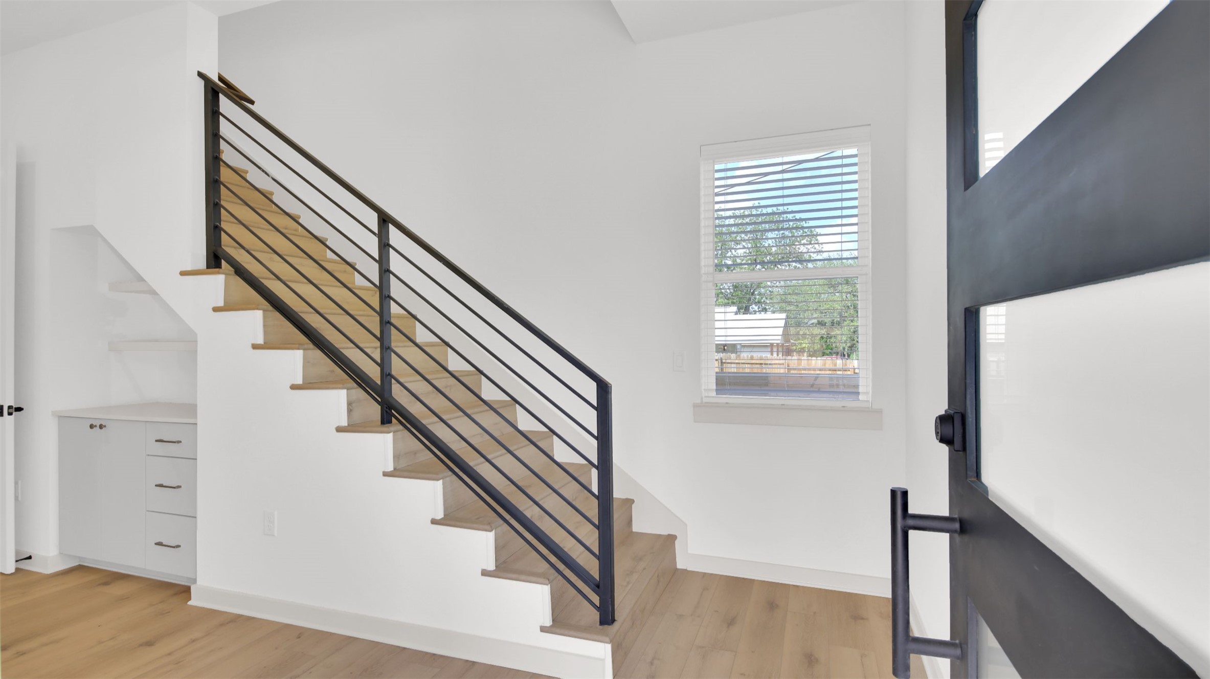 7208 Providence Avenue, Unit 1 Austin, TX 78752 - Photo 23 of 26 Entryway featuring light-toned flooring, white walls, a staircase with a black metal railing, and a window with blinds