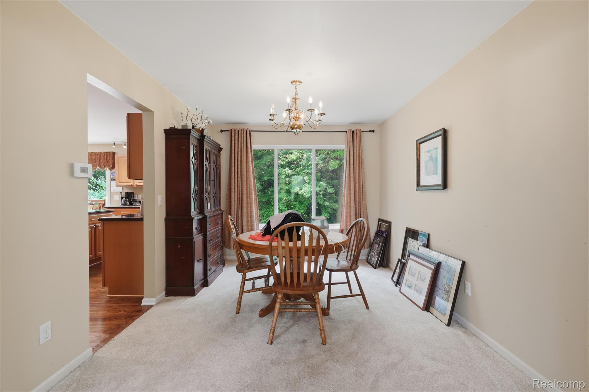 170 Fairhill Way Howell, MI 48843 - Photo 12 of 46 Carpeted dining area featuring a window with exterior tree views, a brass chandelier, and a wide entryway to the kitchen with wood-finish flooring