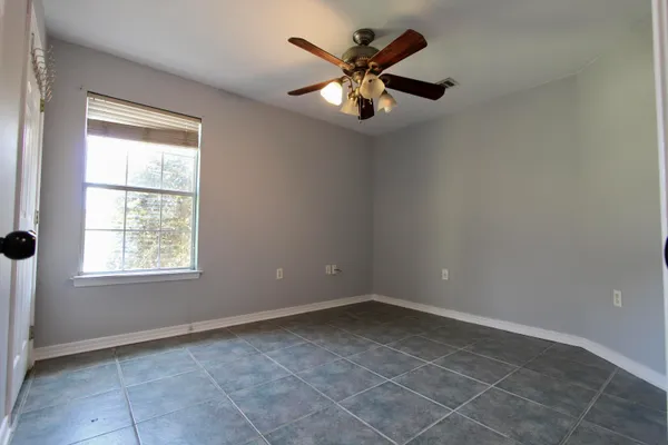 an empty room with chandelier fan and windows