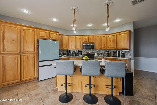 a kitchen with stainless steel appliances granite countertop a stove a refrigerator a kitchen island a dining table and chairs with wooden floor