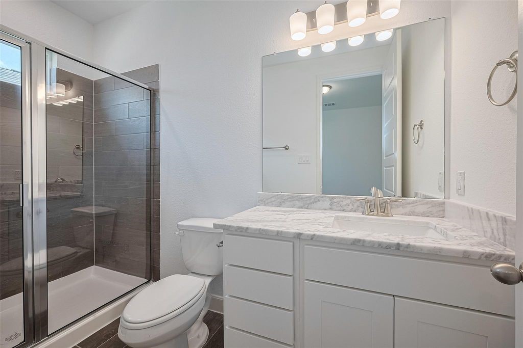 1051 Comal Trail Dayton, TX 77535 - Photo 24 of 49 a bathroom with a granite countertop sink toilet a mirror and shower