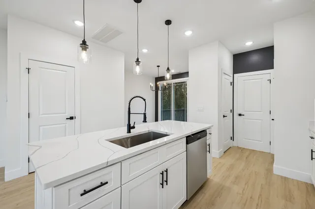 a kitchen with stainless steel appliances a refrigerator a sink and white cabinets with wooden floor