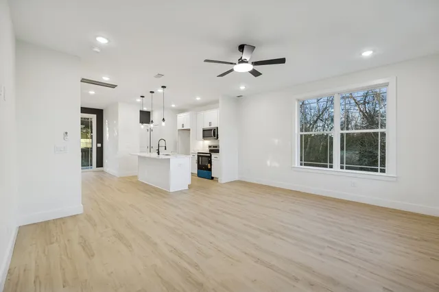 a view of an empty room with a window and kitchen view