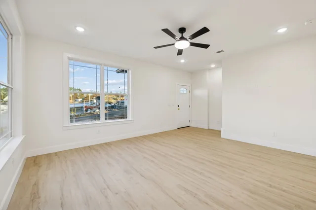 an empty room with wooden floor fan and windows
