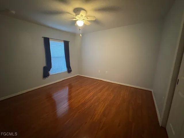an empty room with wooden floor chandelier fan and windows