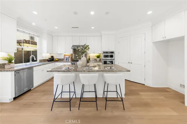a kitchen with stainless steel appliances kitchen island granite countertop a dining table chairs and a refrigerator