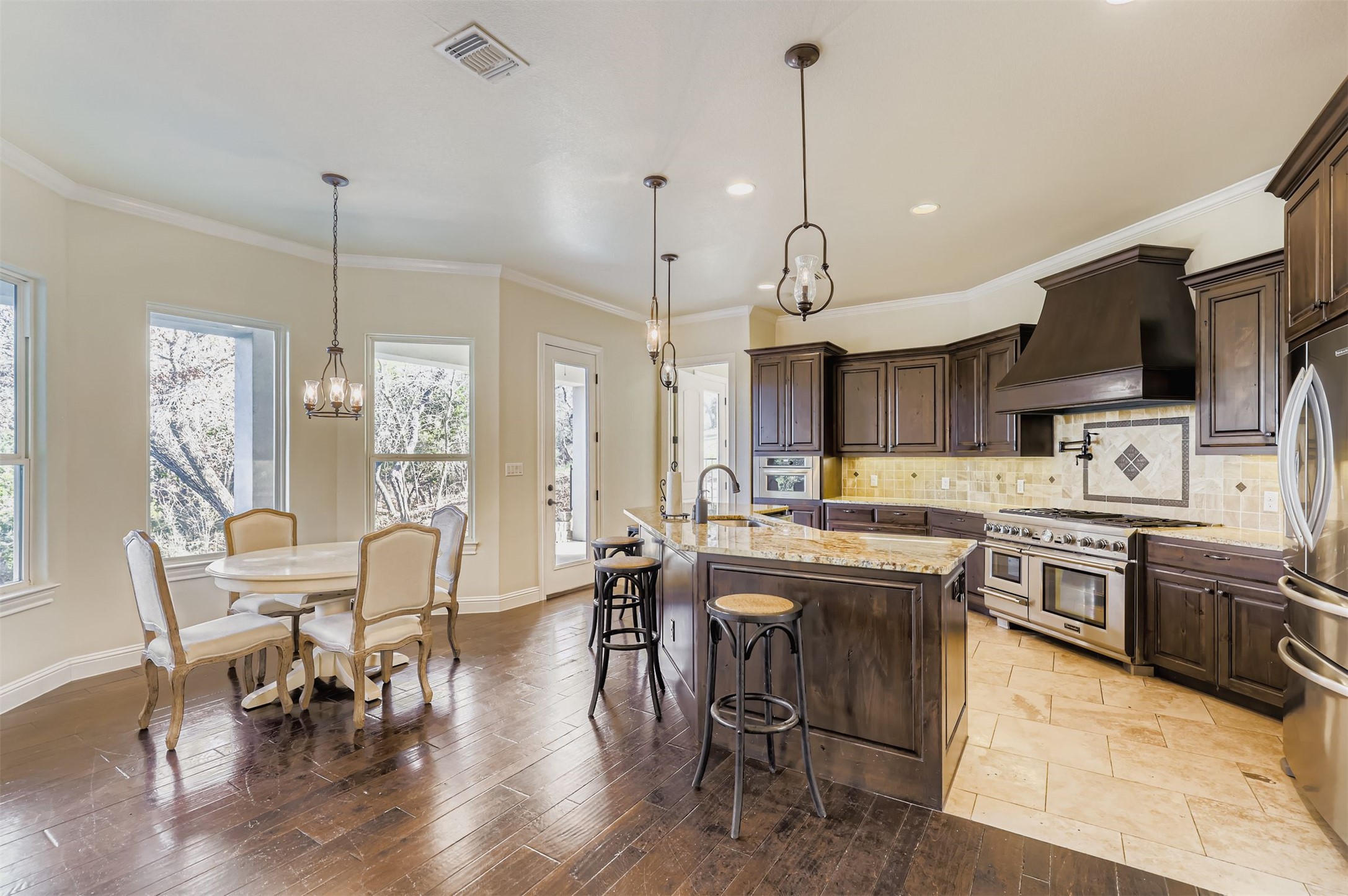 1415 Roaring Fork Leander, TX 78641 - Photo 4 of 39 Kitchen with hanging light fixtures, crown molding, light stone countertops, dark wood cabinetry, and custom range hood