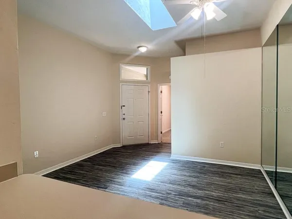 an empty room with wooden floor a chandelier fan and refrigerator