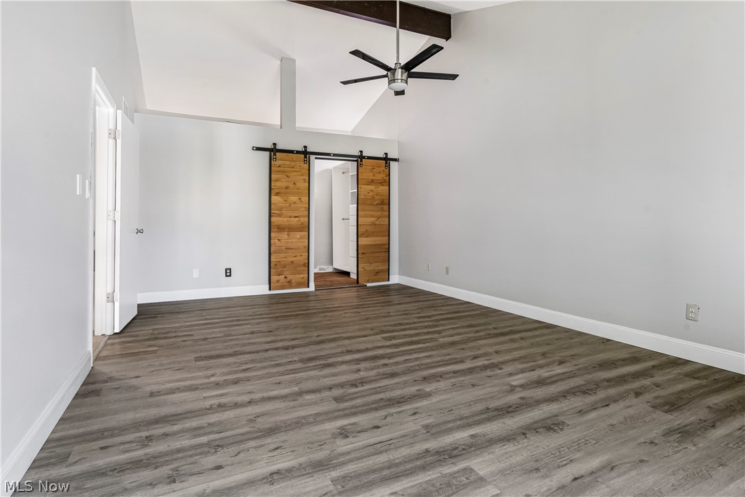 3428 South Smith Road Fairlawn, OH 44333 - Photo 10 of 30 Unfurnished living room with hardwood / wood-style flooring, beam ceiling, a barn door, high vaulted ceiling, and ceiling fan