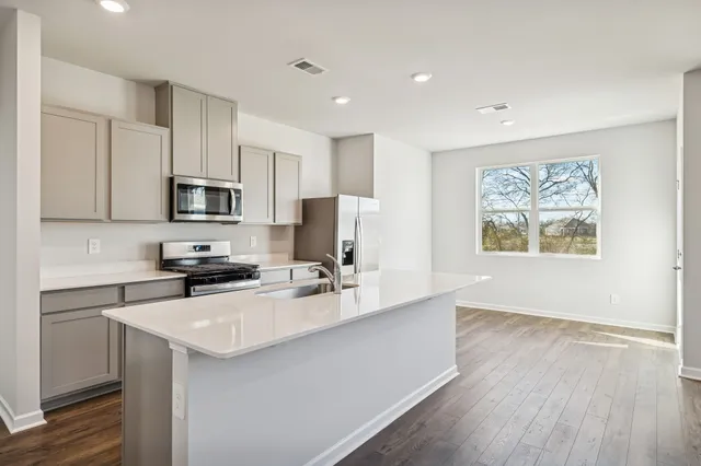 a kitchen with stainless steel appliances a microwave a stove a sink dishwasher a refrigerator and white cabinets with wooden floor