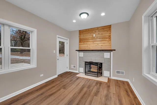 a view of an empty room with wooden floor fireplace and a window
