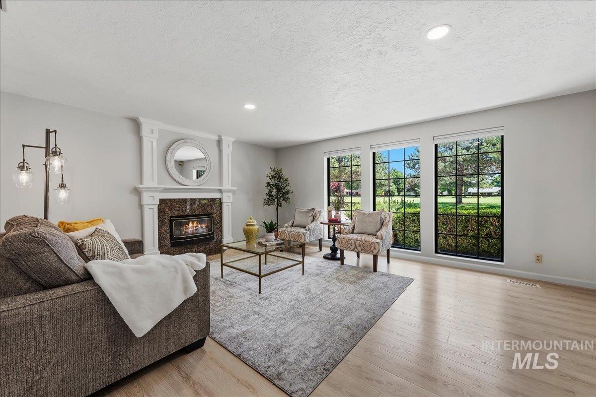599 Pebble Beach Way Eagle, ID 83616 - Photo 18 of 44 Living area featuring light wood-finish flooring, a fireplace with a stone surround and decorative white mantel, and three large windows with black grilles