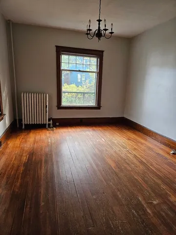an empty room with wooden floor chandelier and windows