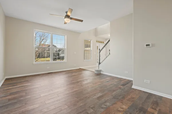 a view of an empty room with wooden floor and a ceiling fan