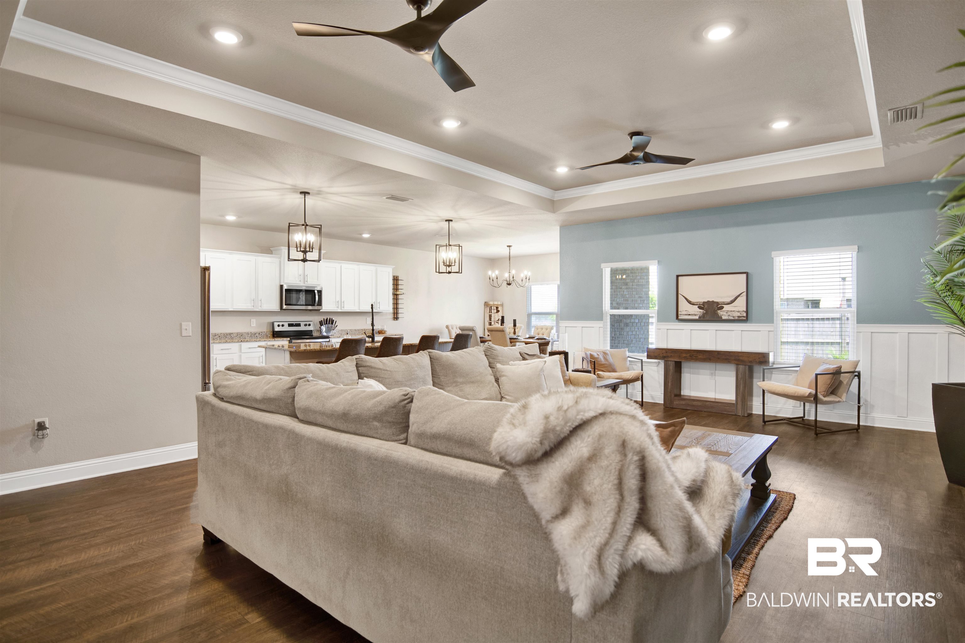 8493 Bronze Lane Foley, AL 36535 - Photo 9 of 38 Spacious living area featuring dark wood-finish flooring, a tray ceiling with recessed lighting and ceiling fans, and wainscoting with a feature wall